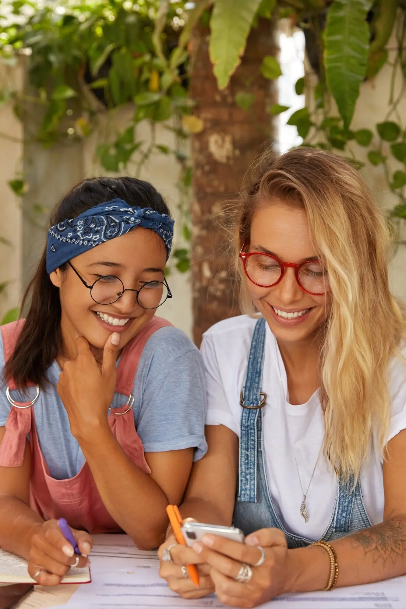 Mixed-race female colleagues are using a modern smartphone to read an online publication.